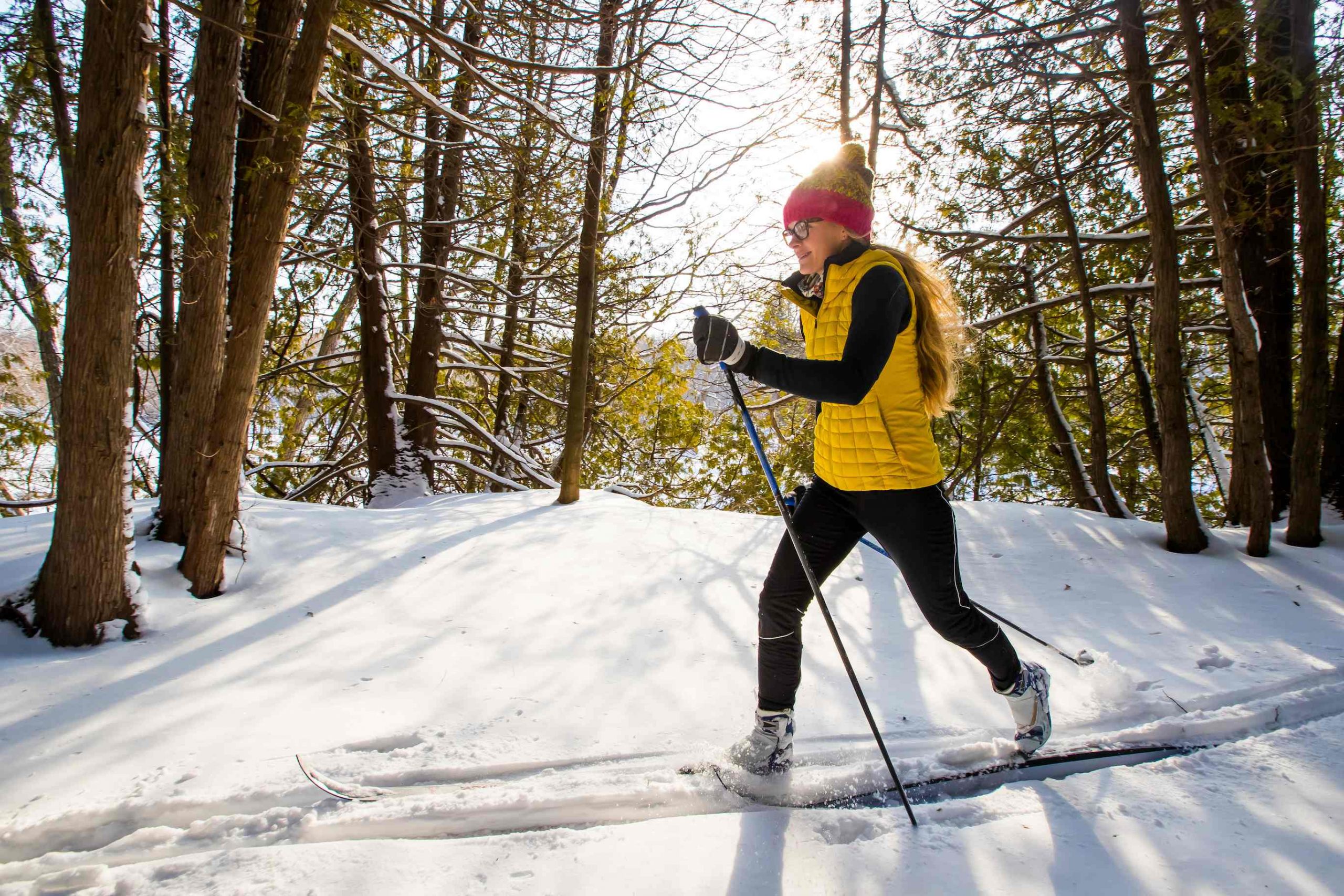A young woman cross country skiing on a path lined with trees