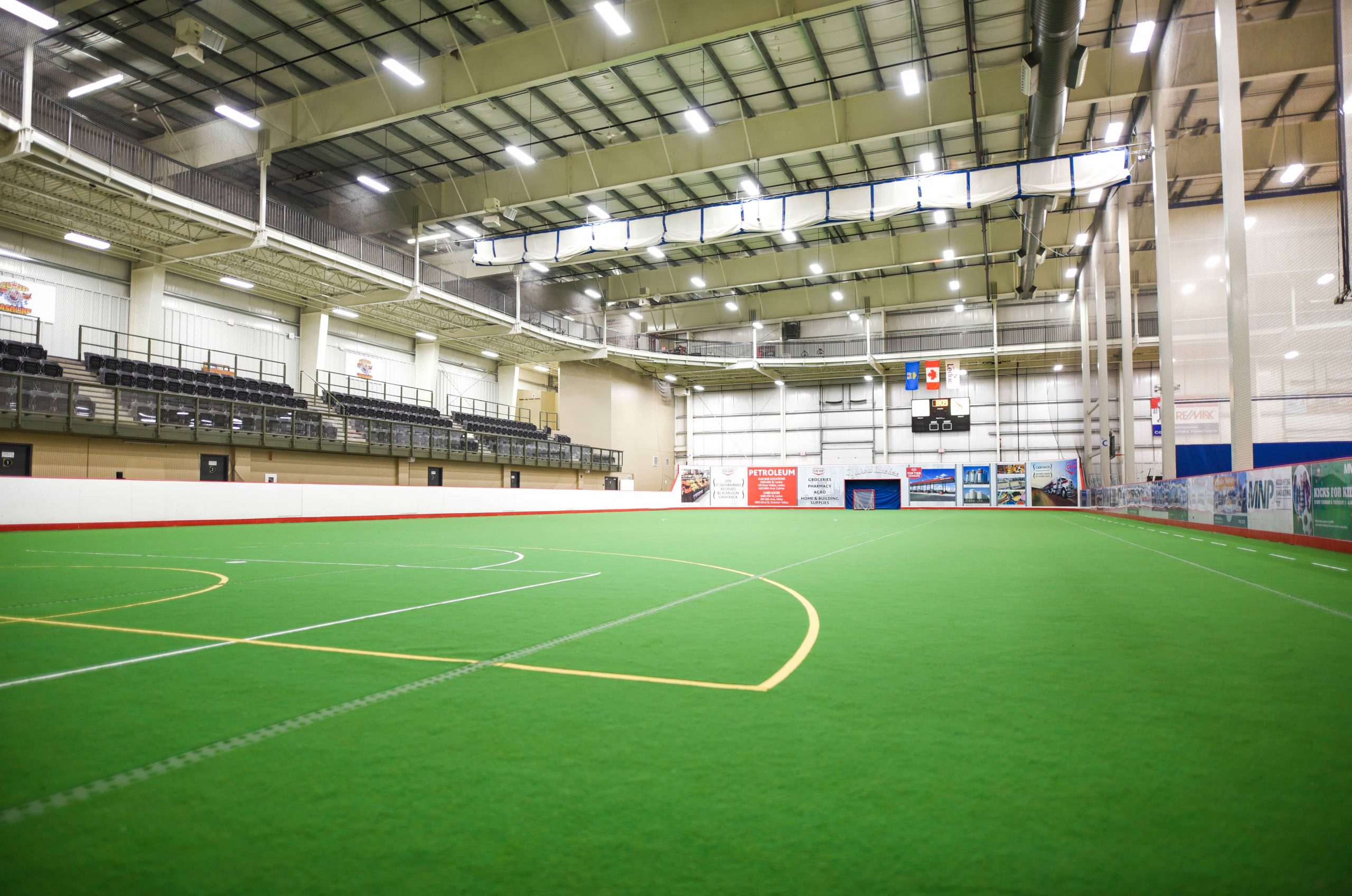http://Indoor%20sports%20facility%20with%20artificial%20turf,%20bleachers%20on%20the%20left,%20overhead%20lighting,%20and%20banners%20on%20the%20walls.