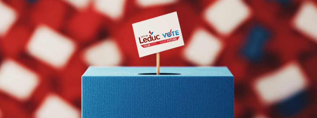 A small sign with "Leduc Vote" is stuck in a blue box, with a blurred red, white, and blue background.