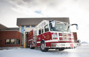 Red fire truck parked on snow outside a modern fire station with a garage.