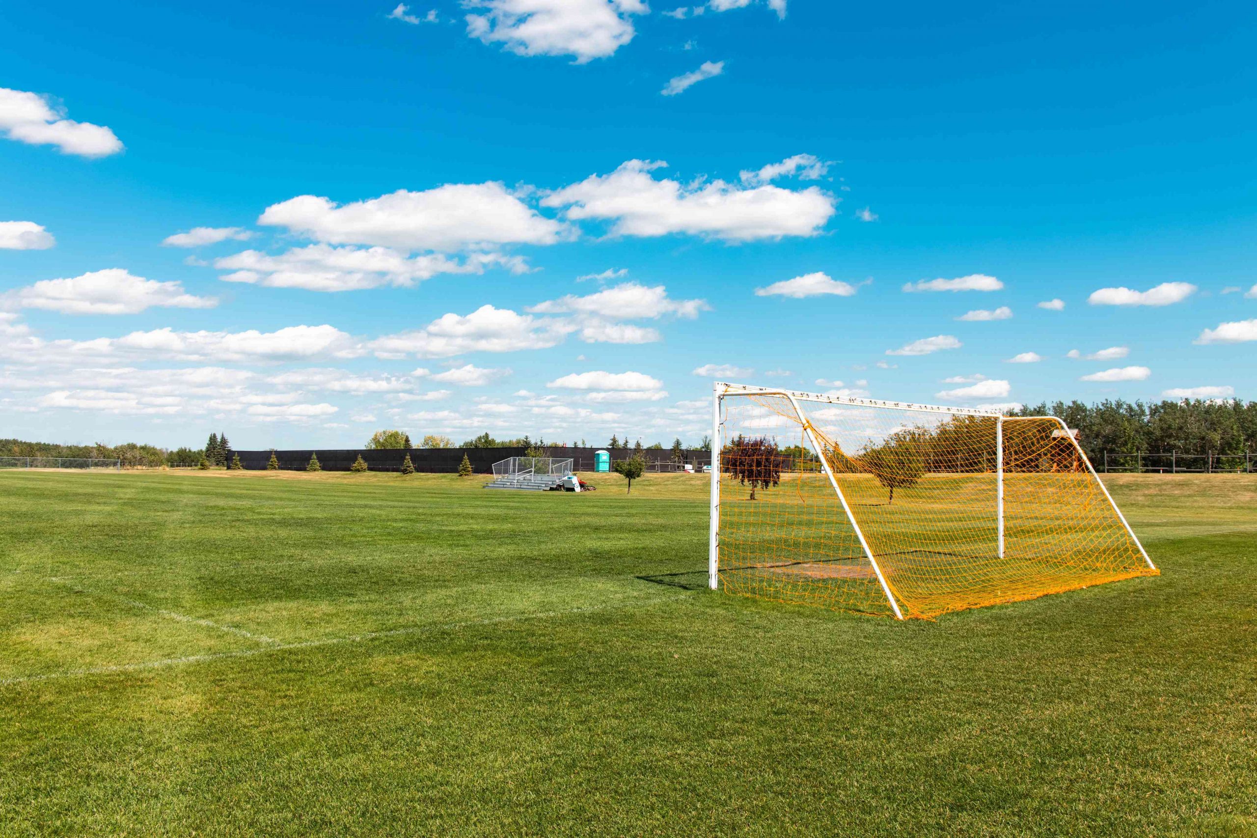 http://Soccer%20field%20with%20a%20goal%20on%20grassy%20terrain%20under%20a%20clear%20blue%20sky%20with%20scattered%20clouds%20and%20trees%20in%20the%20background.