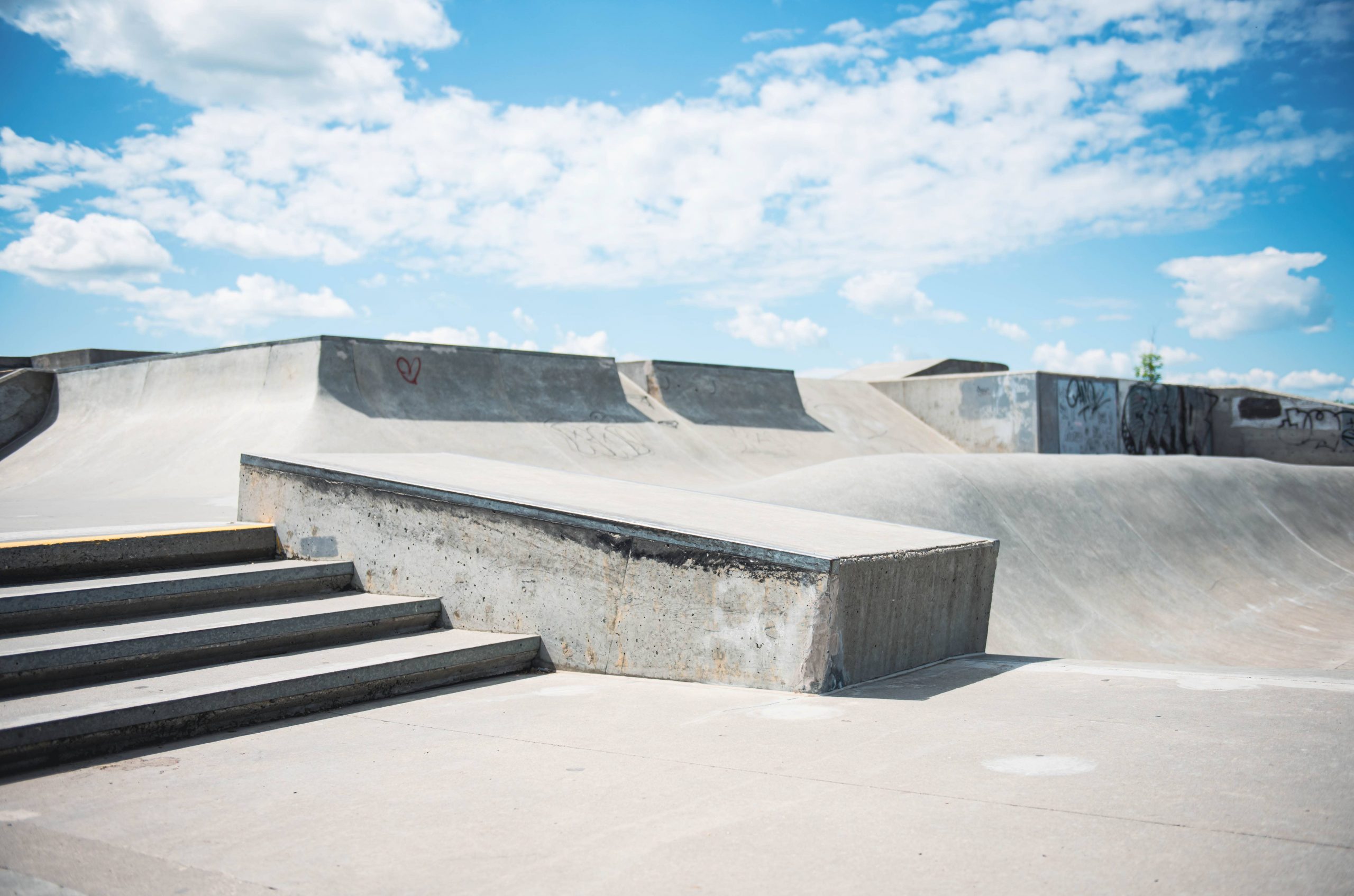 Concrete skate park with various ramps and stairs under a blue sky with scattered clouds.