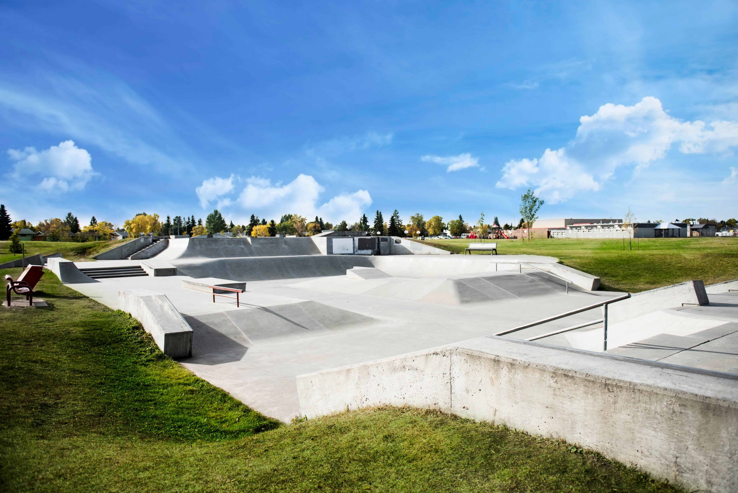 Concrete skatepark under a clear blue sky with surrounding green grass and distant trees.