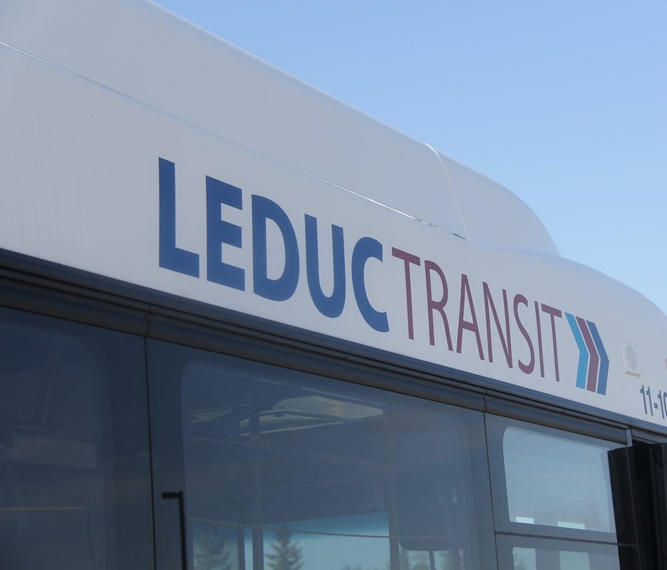 http://Side%20view%20of%20a%20bus%20with%20Leduc%20Transit%20written%20in%20blue%20and%20red%20letters%20against%20a%20clear%20blue%20sky.