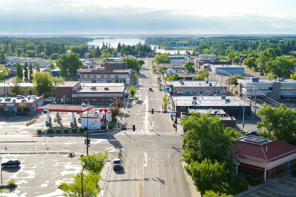 Aerial view of Leduc with intersecting roads, buildings, trees, and distant water under a partly cloudy sky.