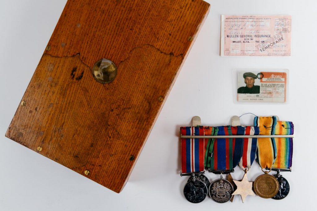 Wooden box, insurance card, ID card, and five military medals with colorful ribbons displayed on a white surface.