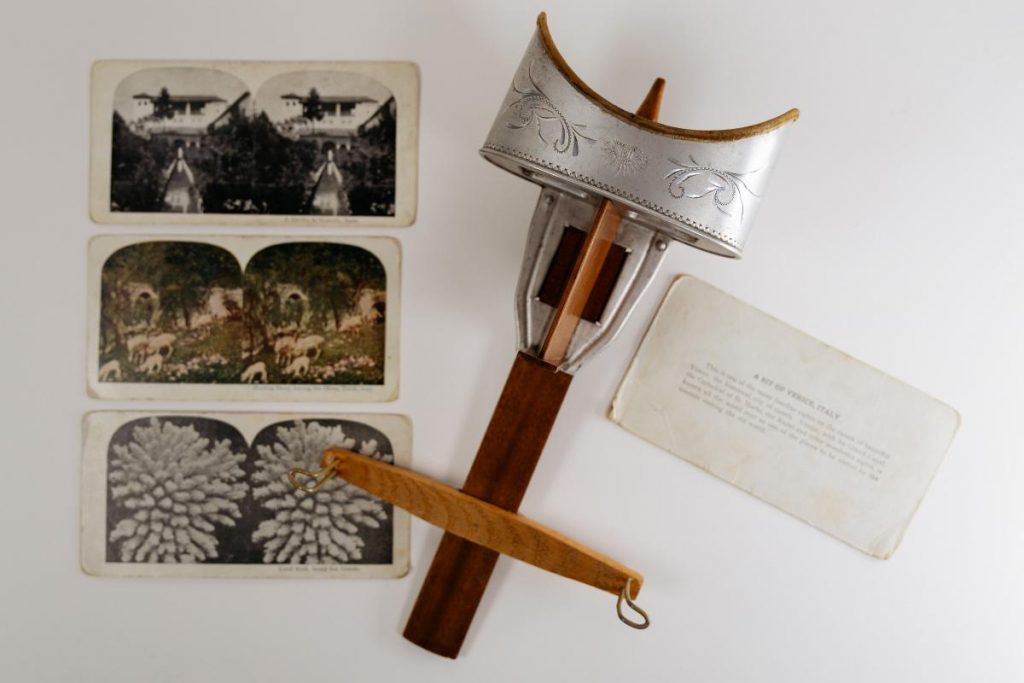 A vintage hand-held stereoscope beside illustrated cards.