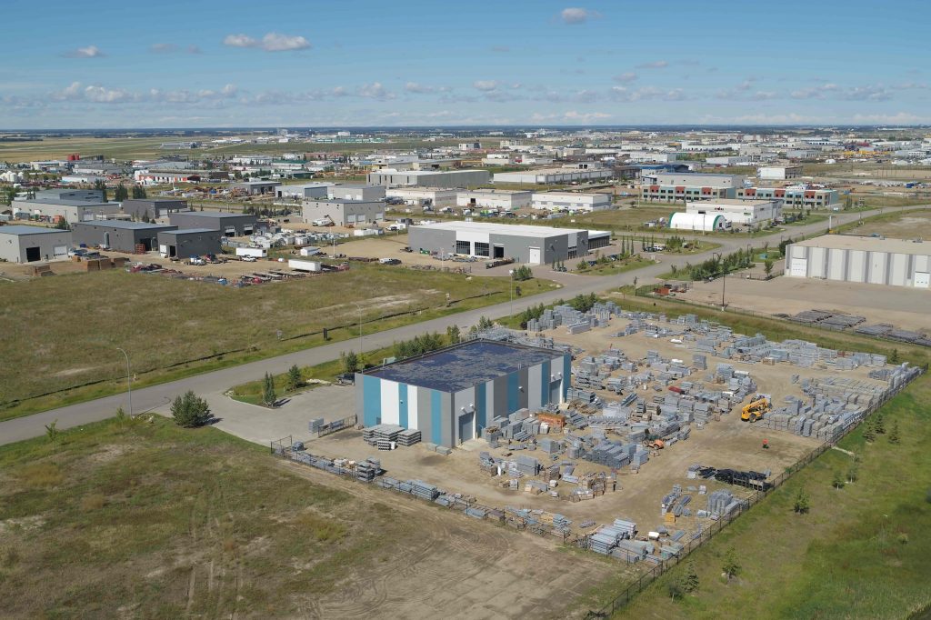 Aerial view of an industrial area with warehouses, storage facilities, and scattered construction materials on a clear day.