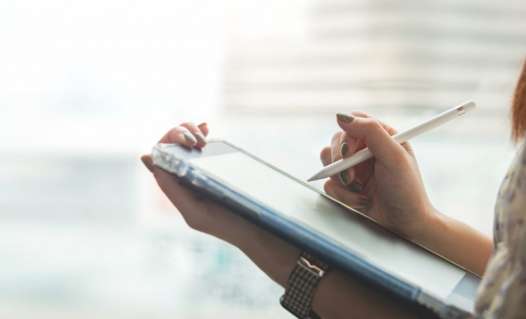 Person holding a tablet and using a stylus to write, with a blurred background.