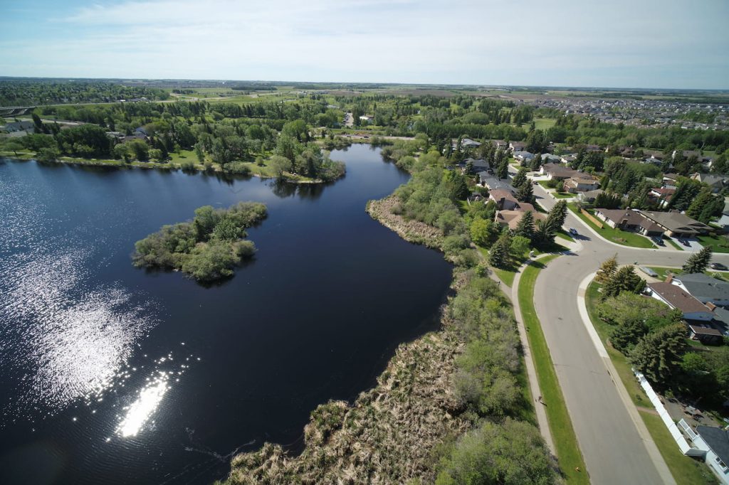 Aerial view of a suburban lakeside neighborhood with houses, roads, and abundant greenery on a clear day.