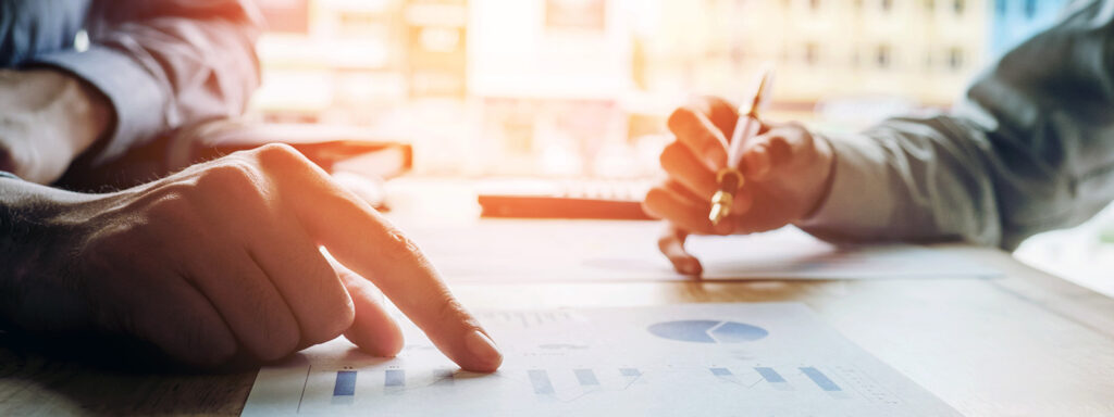 Close-up of two people reviewing documents with charts and graphs, pointing and writing notes during a planning or analysis meeting