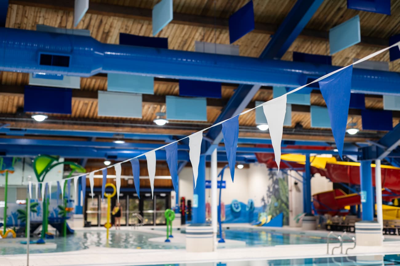 http://Indoor%20swimming%20pool%20with%20blue%20and%20white%20pennant%20flags,%20colorful%20water%20play%20structures,%20and%20tunnel%20slides%20in%20the%20background.