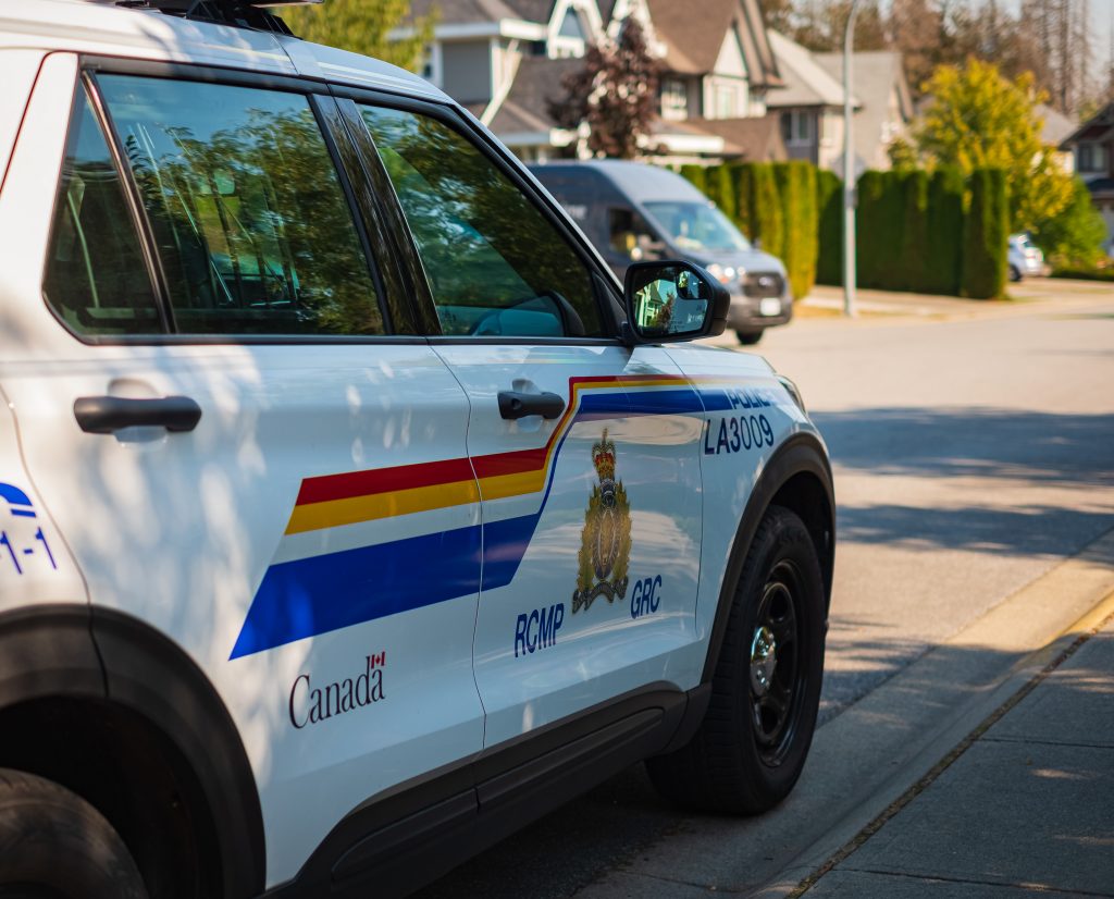 RCMP police vehicle parked on a residential street, with houses and trees visible in the background.