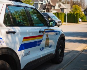 RCMP police vehicle parked on a residential street, with houses and trees visible in the background.