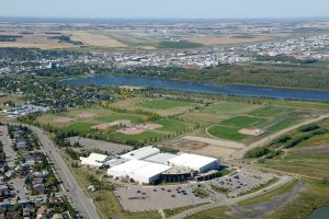 Aerial view of a sports complex with baseball fields, near a river, surrounded by residential areas and open fields.