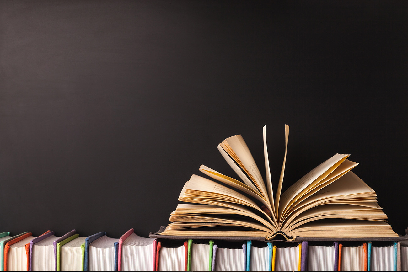 Stock photo of a row of books, with a book opened stacked on top.