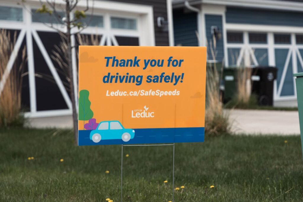 Orange and blue sign that reads 'thank you for driving safely' located on the front lawn at a residential home in Leduc.