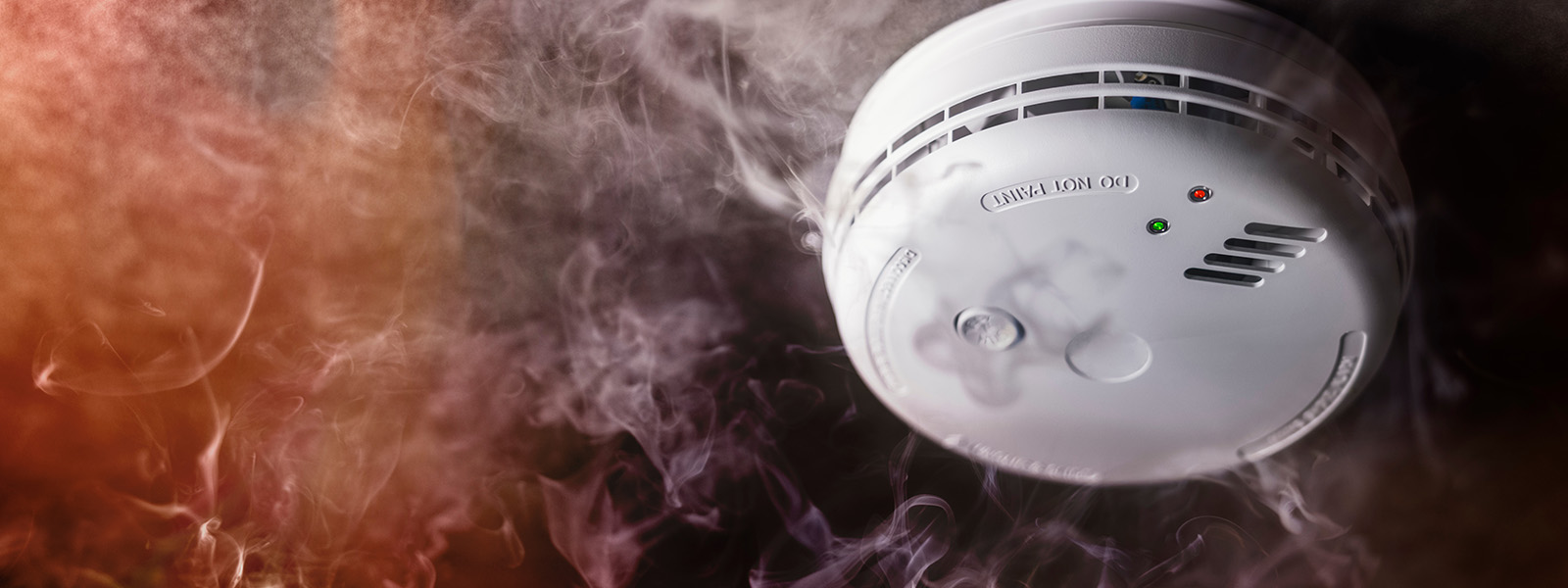 http://Image%20of%20a%20smoke%20detector%20with%20smoke%20and%20fire%20growing%20in%20the%20background.