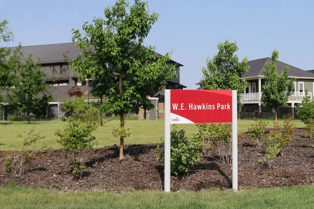 New W.E. Hawkins Park sign installed in the Woodbend neighbourhood, with landscaped green space and nearby homes in the background.