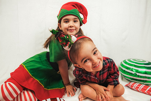 Two children dressed in festive elf costumes pose together during a Little Elves program activity.